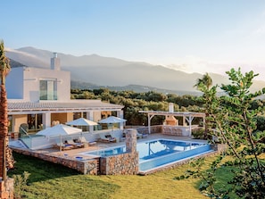 A modern house with a swimming pool, outdoor seating, and a view of mountains. - Beautiful Luxe Villa in Private Olive Grove, sea and Mountain View, Close to sea (Agios Nikolaos)