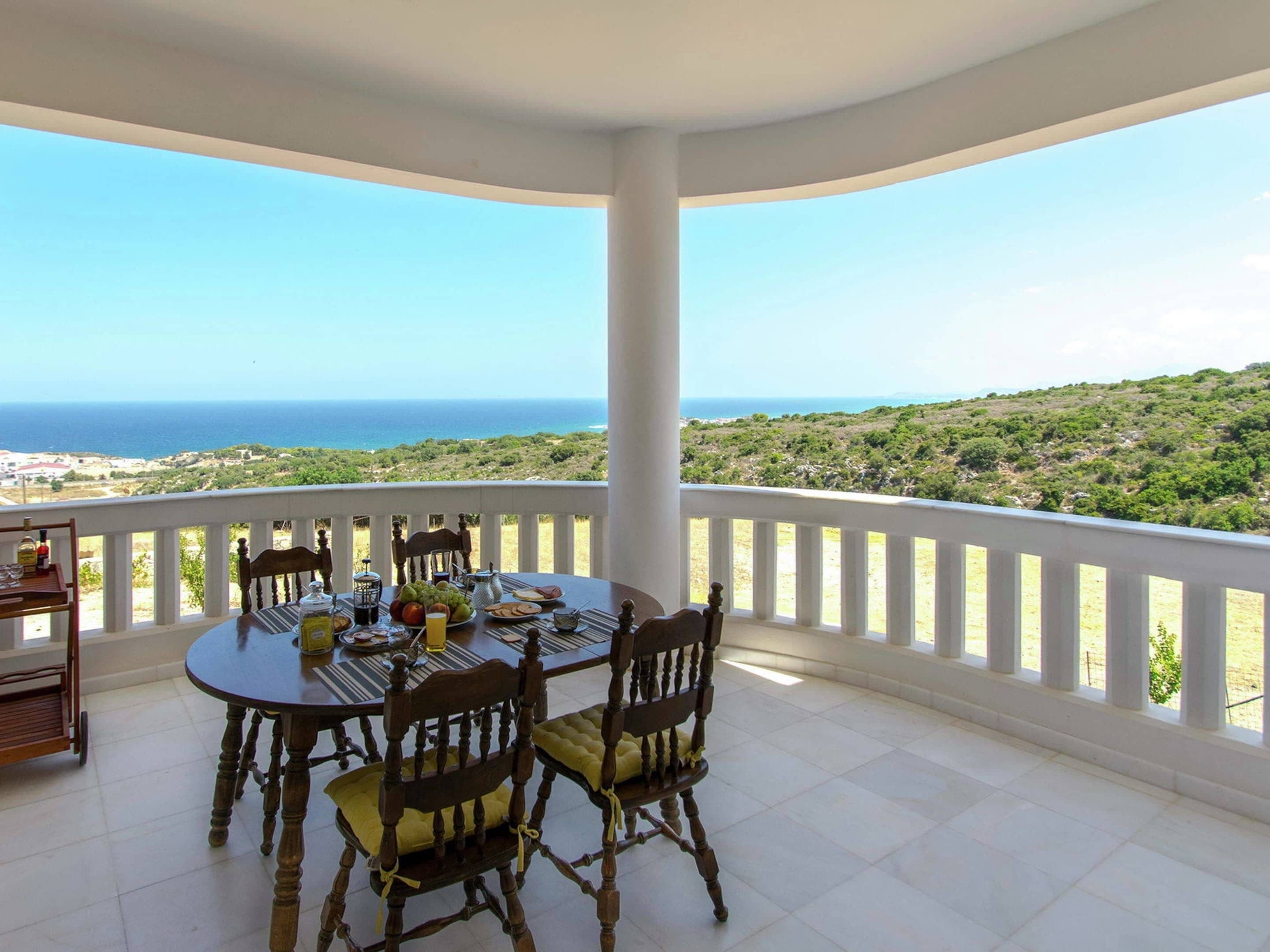 A round table with chairs on a balcony overlooking a coastal landscape.