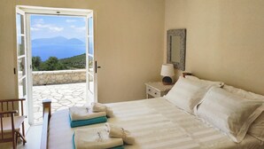 A bedroom with a bed, a nightstand, a lamp, a mirror, and a view of the sea through an open door. - Spacious Villa in Vasiliki with Swimming Pool & Hot Tub (Lefkada)