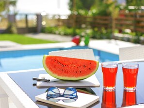 A poolside setting with a watermelon, glasses, and a pen on a table.