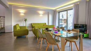 Ein modernes Wohnzimmer mit einem Glastisch, grünen Sofas und einem Fernseher.
