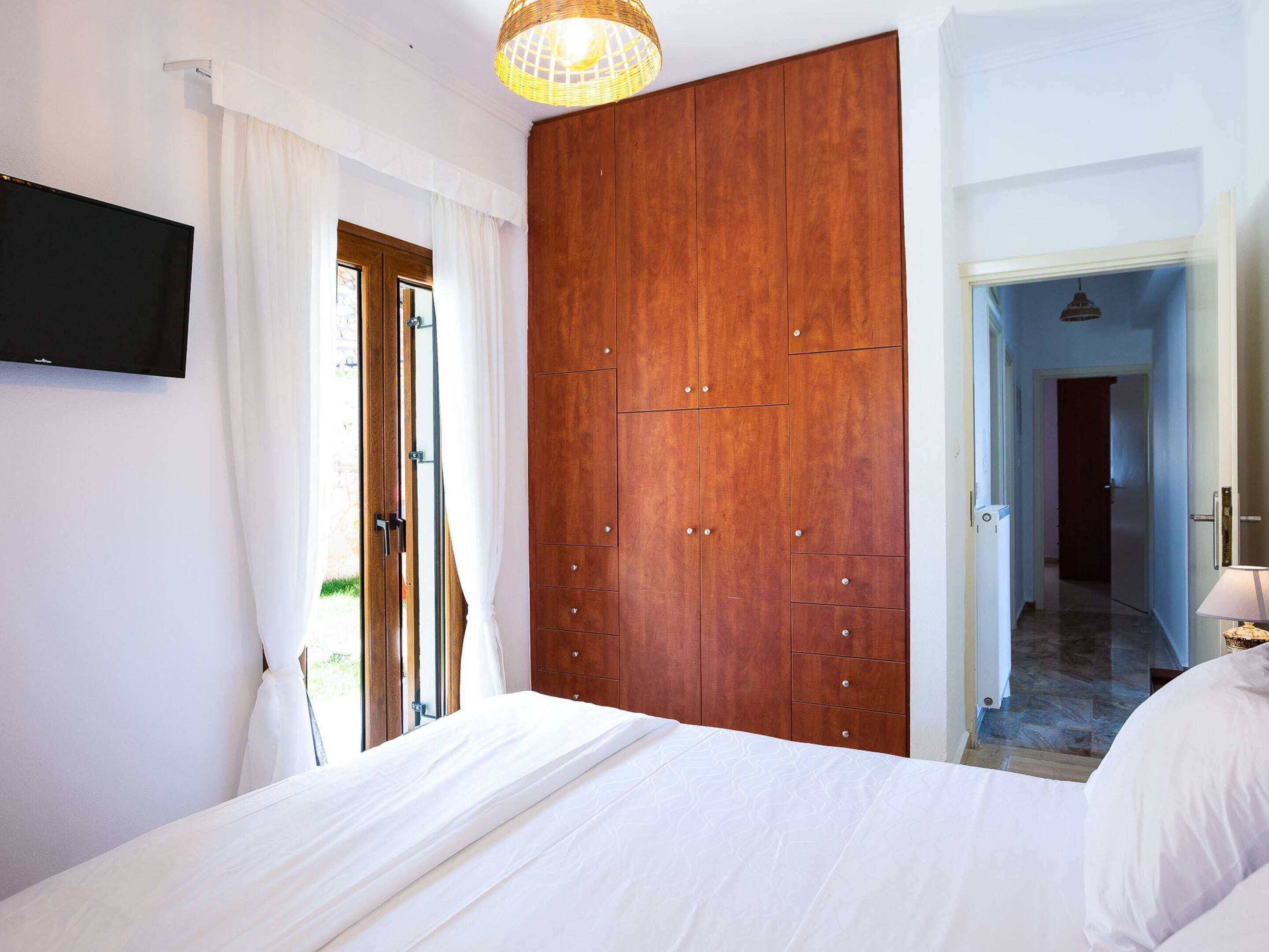 A bedroom with a large bed, wooden wardrobe, and a television on the wall.