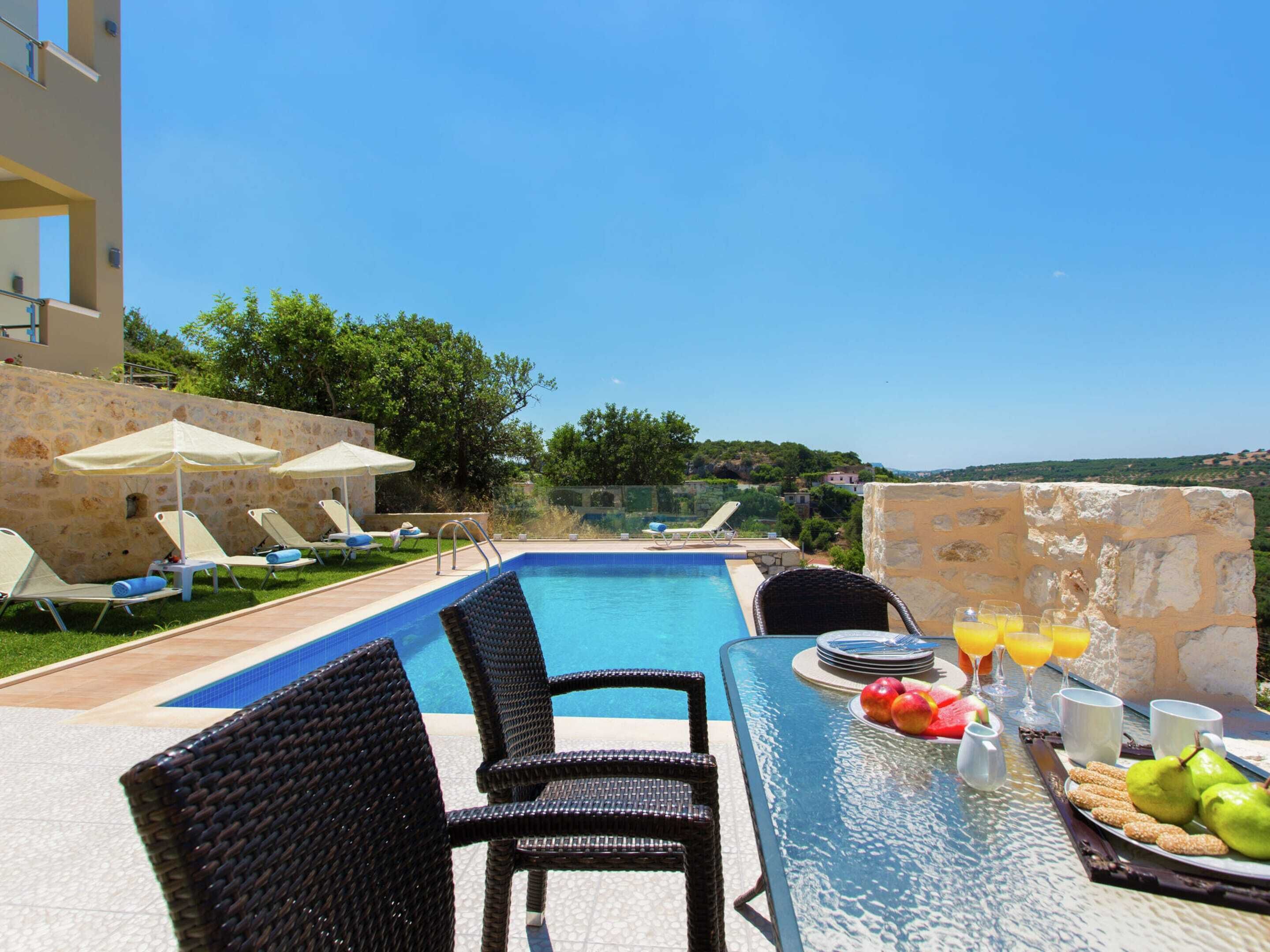 A poolside area with lounge chairs, a table with breakfast items, and a clear view of the surrounding landscape.