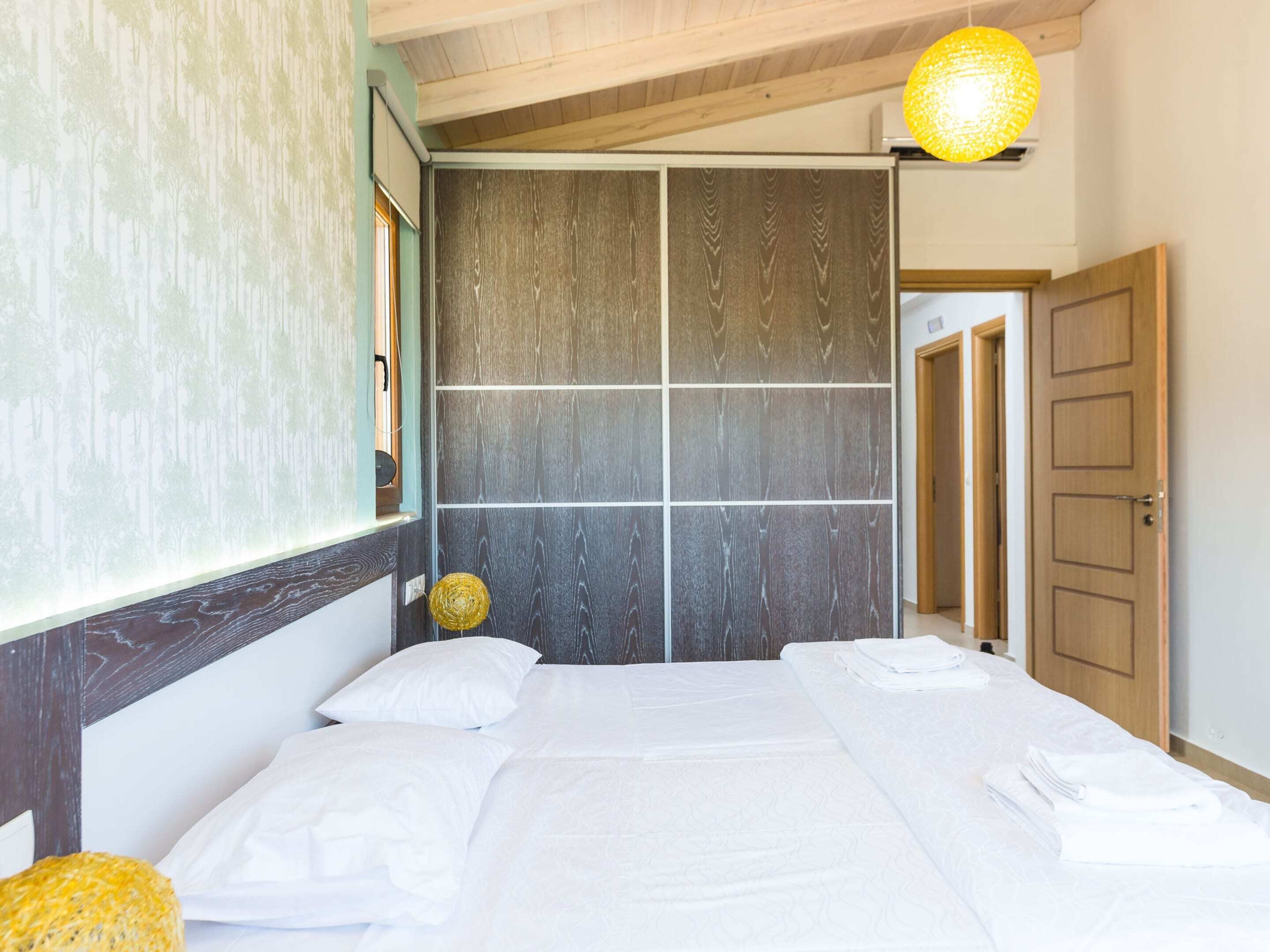 A bedroom with a large bed, a wooden headboard, a wall with a grid pattern, and a hanging light fixture.