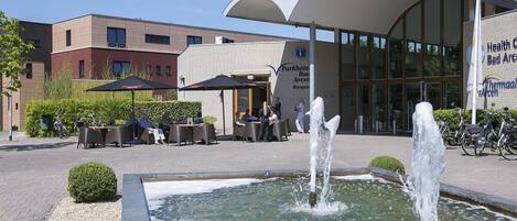 Un espacio al aire libre con mesas y sillas, una fuente y un edificio con el letrero de un centro de salud.