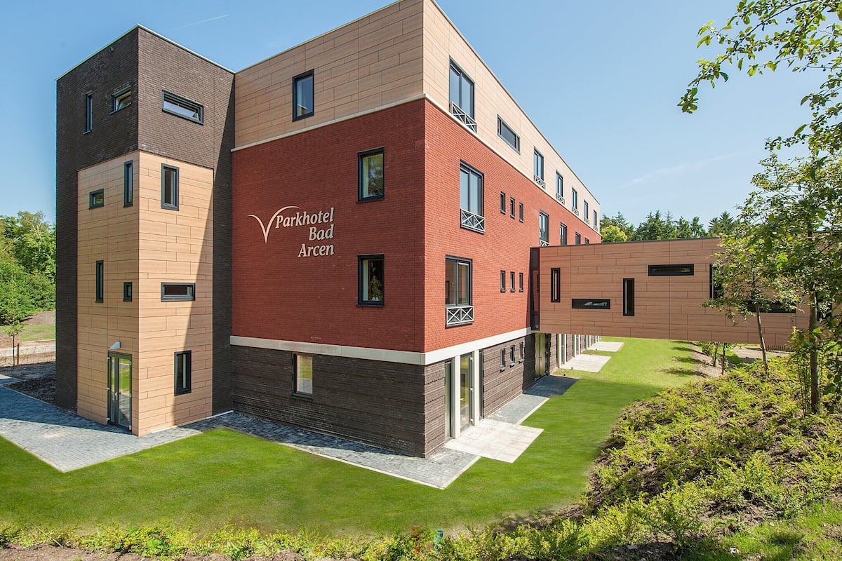 A modern hotel building with a mix of brick and wood panel facades, labeled "Parkhotel Bad Arcen."