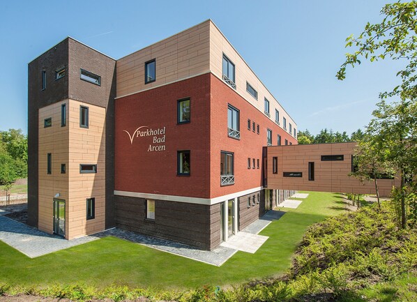 Een modern hotelgebouw met een gevel van baksteen en houten panelen, met de tekst 'Parkhotel Bad Arcen'.