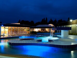 Een modern buitenzwembad met een waterval, een lounge met glazen wanden en een overdekt zitgedeelte.