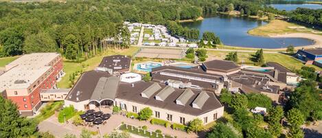 An aerial view of a hotel with multiple buildings, a swimming pool, and a lake in the background.