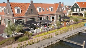 A row of traditional Dutch houses with red-tiled roofs, outdoor seating areas, and a canal in the foreground.