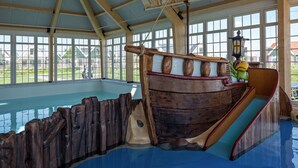 A large indoor swimming pool with a wooden ship structure and a slide.