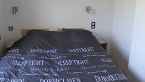 A bedroom with a bed covered in a blanket with text, two bedside tables, and wall-mounted lights. - Chalet in Friesland Near Nature Reserves (De Veenhoop)