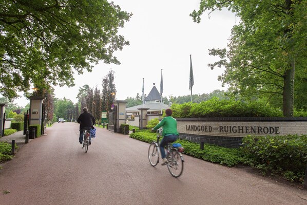 A pathway with cyclists, a sign reading "Landgoed-Ruighenrode", and a building with a dome in the background.