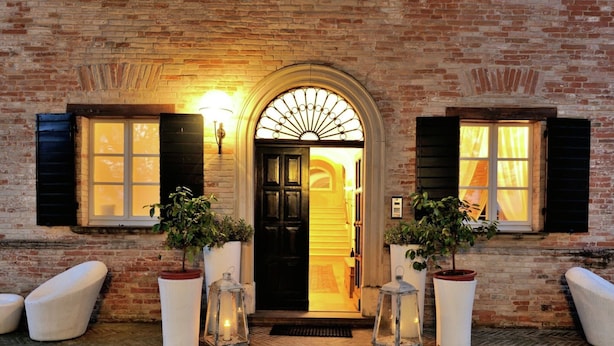 A brick building with a black door, two potted plants, and two wicker chairs. - Villa in Montemaggiore With Private Pool (Colli al Metauro)