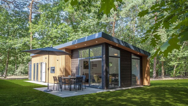 Ein modernes Haus mit Terrasse, großen Fenstern und Blick auf den umliegenden Wald.