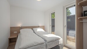Ein Schlafzimmer mit Bett, Nachttisch, Holz-Kopfteil, einer Schiebetür zum Außenbereich und einer Deckenleuchte.