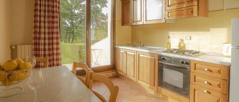 A kitchen with wooden cabinets, a tiled backsplash, a stove, and a dining table with chairs.