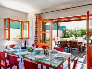 A dining area with a glass table set for six, red chairs, and a view of the garden through large windows.