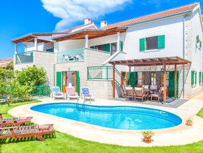 A two-story house with a swimming pool, outdoor seating, and a covered patio.