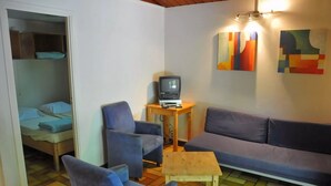 A small, cozy room with a sofa, two armchairs, a small table, a television, and a bed in the corner. - Cozy, Wooden Chalet With a Microwave, Located in a Forest (Viroinval)