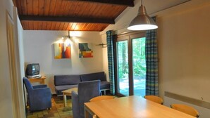 A dining area with a wooden table and chairs, a sofa, and a television on a small table. - Cozy, Wooden Chalet With a Microwave, Located in a Forest (Viroinval)