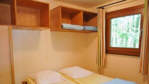 A small, single-bed room with a wooden headboard, a window with curtains, and a shelf above the bed. - Cozy, Wooden Chalet With a Microwave, Located in a Forest (Viroinval)