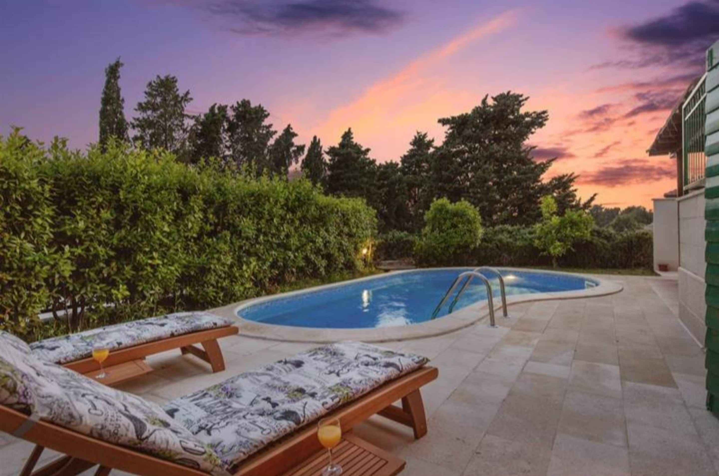 A swimming pool with lounge chairs and a sunset view.