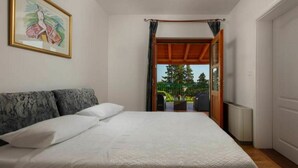 A bedroom with a bed, a painting, and a view of a garden through an open door.
