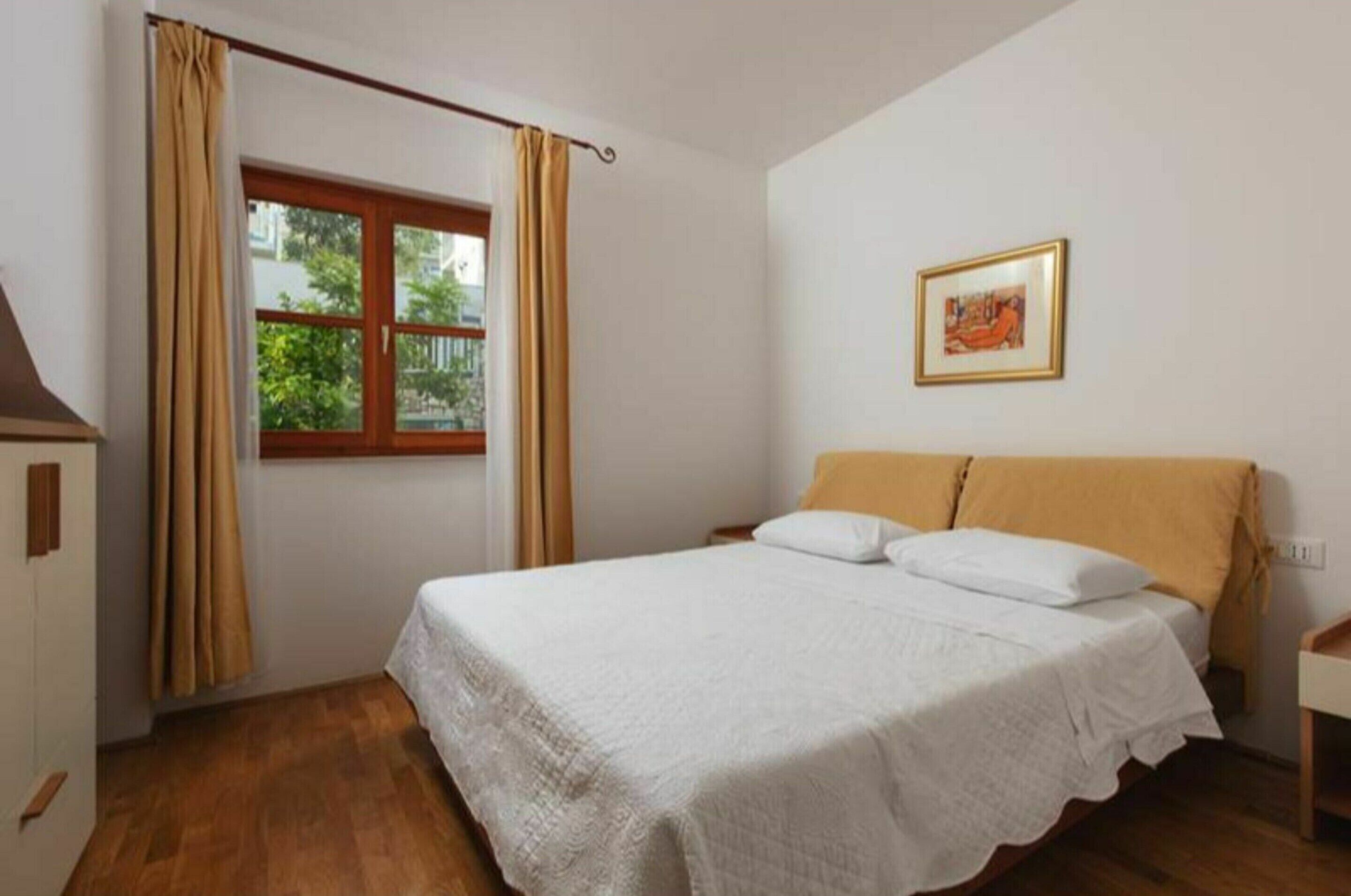 A bedroom with a bed, curtains, a window, and a framed picture on the wall.