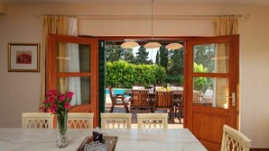 An open-plan living area with a dining table, chairs, and a view of a swimming pool.