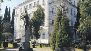 Un grand bâtiment blanc, orné d’une statue à l’avant, entouré d’arbres et agrémenté d’un banc.