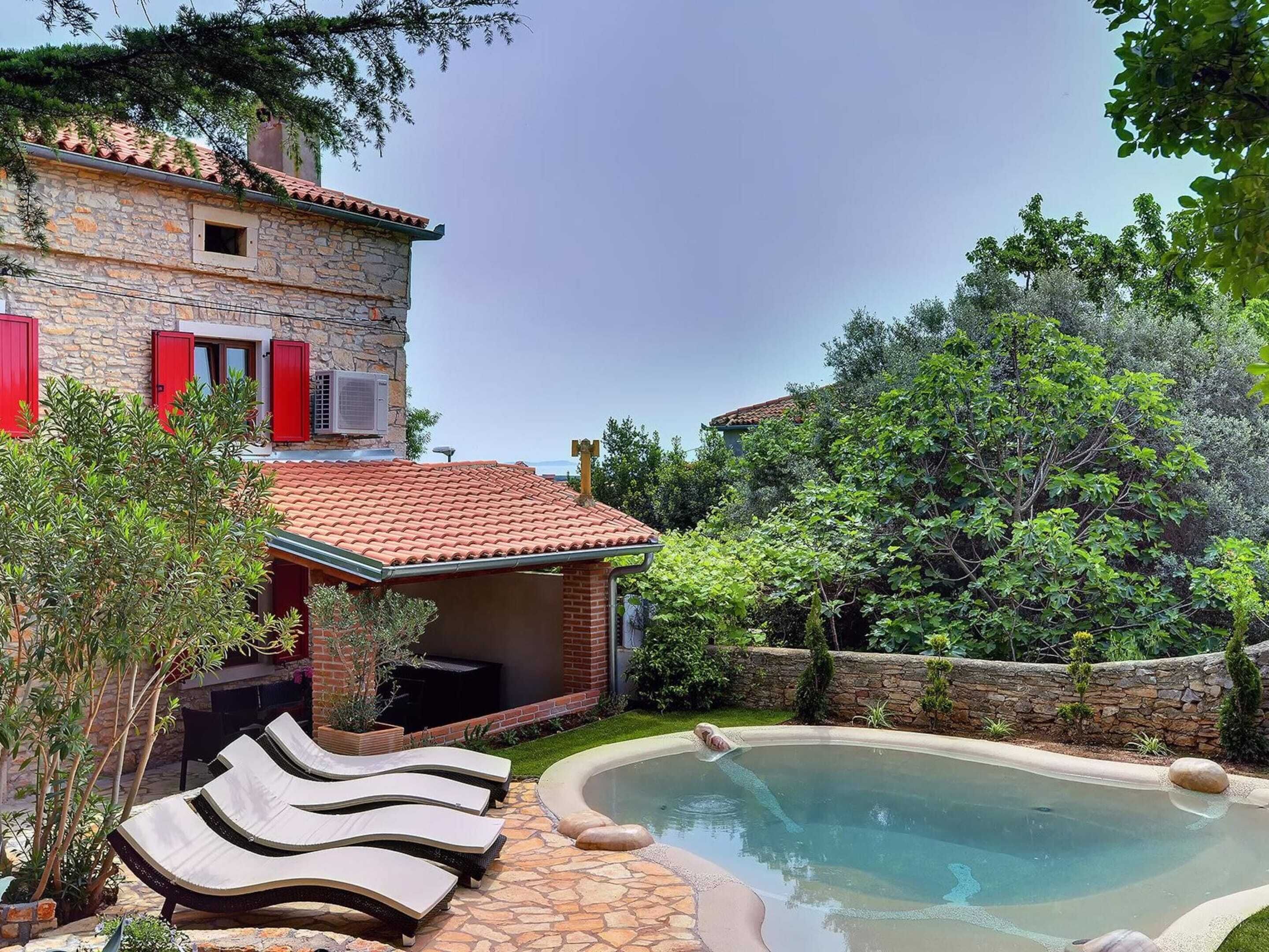 A stone house with a swimming pool, outdoor lounge chairs, and a garden.