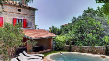 A stone house with a swimming pool, outdoor lounge chairs, and a garden.