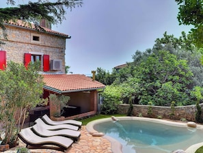 Une maison en pierre avec une piscine, des fauteuils de jardin et un jardin.