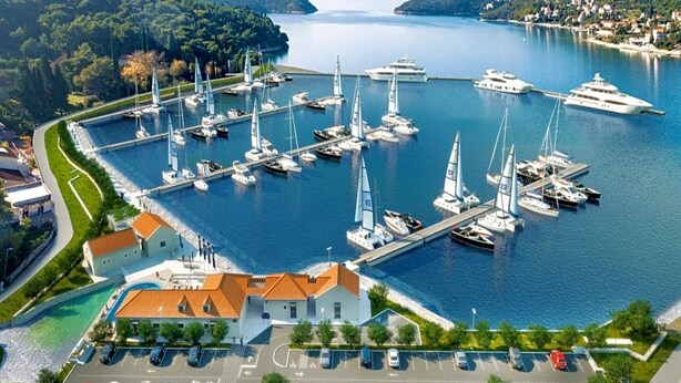Un port de plaisance où sont amarrés de nombreux bateaux, un parking avec plusieurs voitures et un bâtiment doté d’un toit rouge.