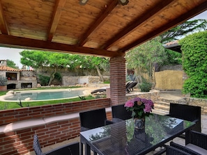 Un patio couvert avec une table et des chaises en verre, un mur en briques et une piscine.