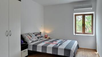 A bedroom with a bed, a wardrobe, a nightstand, a lamp, and a window with a view of trees.