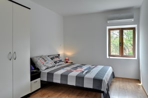 Une chambre à coucher comprenant un lit, une armoire, une table de chevet, une lampe et une fenêtre donnant sur des arbres.
