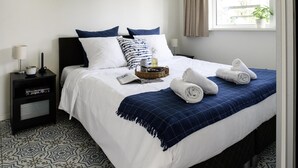 A neatly made bed with white and blue bedding, a blue throw blanket, and two towels. There is a bedside table with a lamp and a small plant. The room has patterned floor tiles. - Penthouse Near Loosdrechtse Lakes (Loosdrecht)