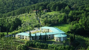 A large, modern building with multiple sections, surrounded by lush green fields and trees.
