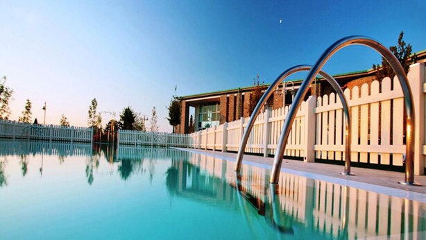 A swimming pool with clear water, metal pool ladders, and a white fence.