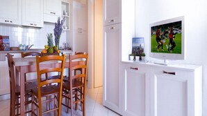A modern kitchen with white cabinets, a dining table with wooden chairs, and a flat-screen TV mounted on a white cabinet.