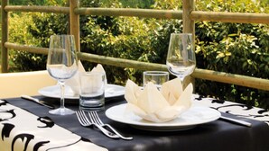 A table set for two with wine glasses, water glasses, and plates, overlooking a lush garden.