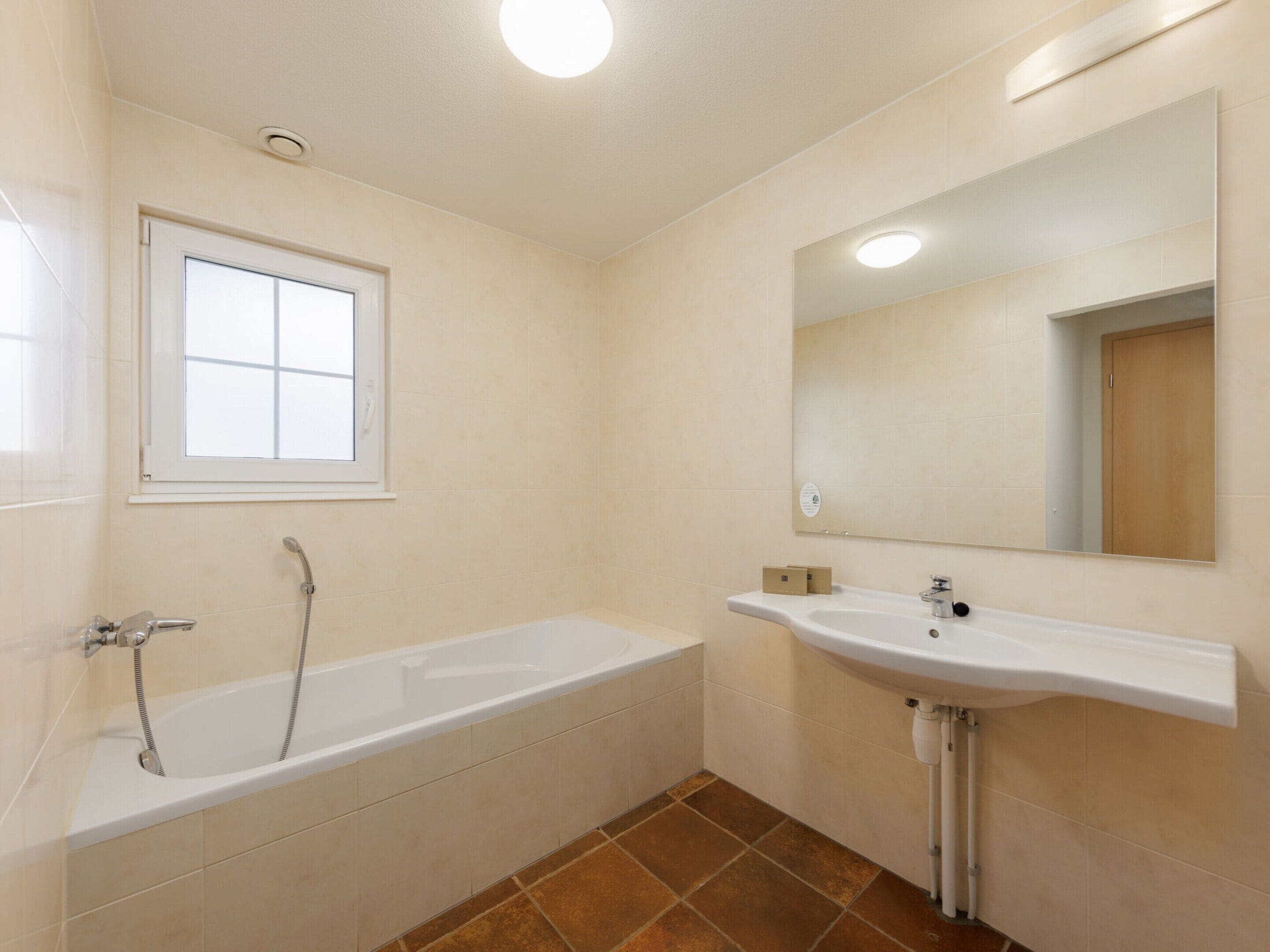 Een badkamer met een bad, een wastafel, een raam en een spiegel.