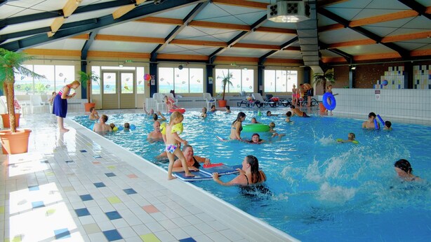 Una piscina interior con varias pistas, suelo de baldosas y un techo alto con vigas de madera.