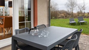 Un patio al aire libre con una mesa y sillas, un jarro de vidrio y dos sillones de lounge al fondo.