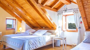 Un dormitorio acogedor en el ático, con techo de madera, una cama con colcha blanca, una mesita de noche pequeña y una ventana con cortinas.