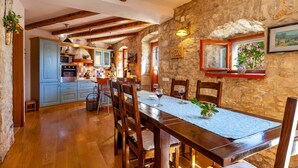 Una cocina rústica con paredes de piedra, vigas de madera y un comedor con una mesa dispuesta para dos.