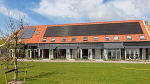 A modern building with a flat roof, solar panels, and a large grassy area in front. - Holiday Home in Oostkapelle Near Beaches (Oostkapelle)