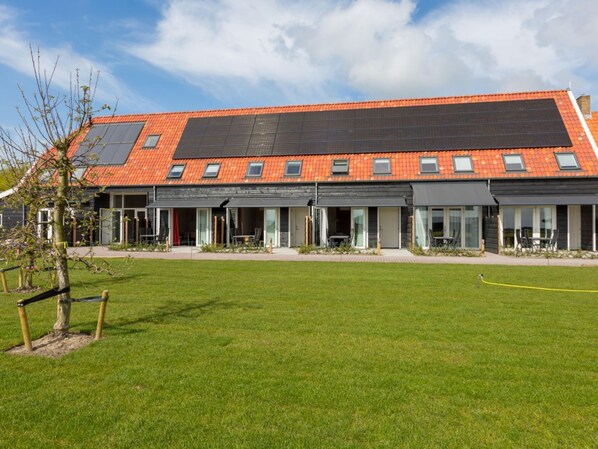 Een modern gebouw met een plat dak, zonnepanelen en een groot gazon ervoor.
